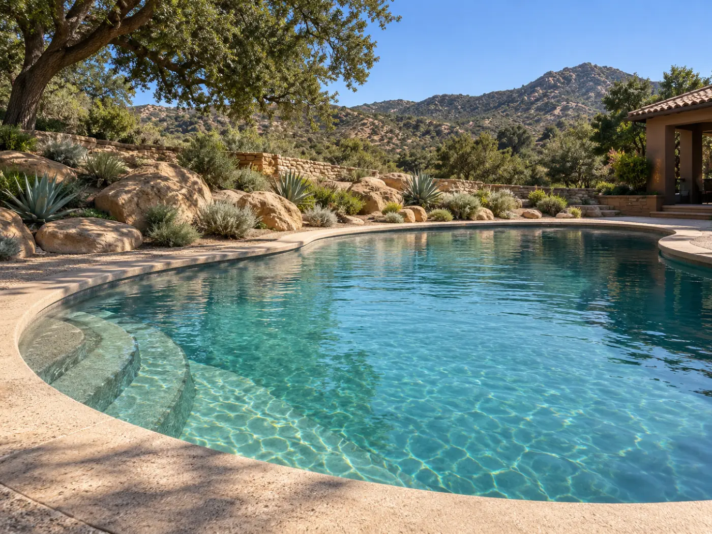 Curved swimming pool with entry steps, boulder landscaping and an oak tree overlooking the hills.
