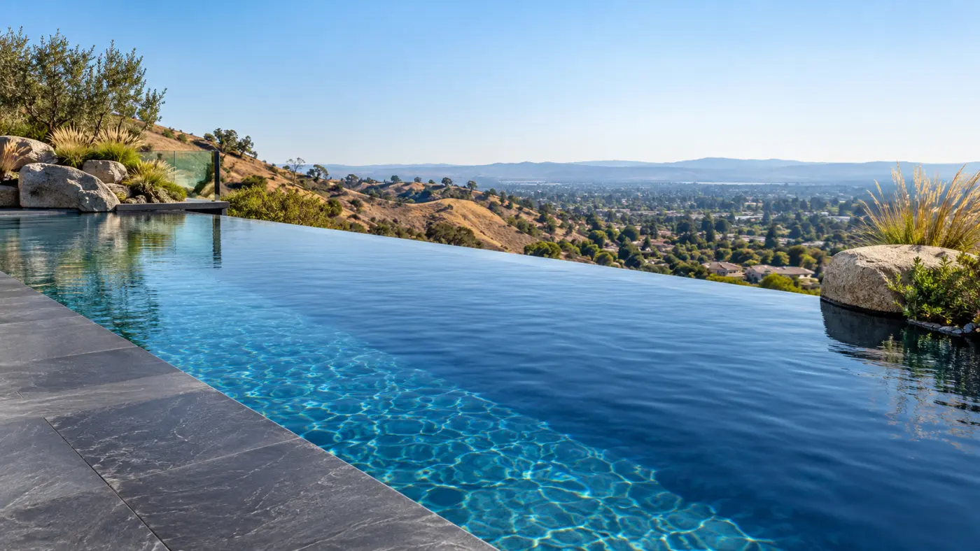 Infinity edge pool with dark stone decking and boulders overlooking a valley view in West Hills, CA.